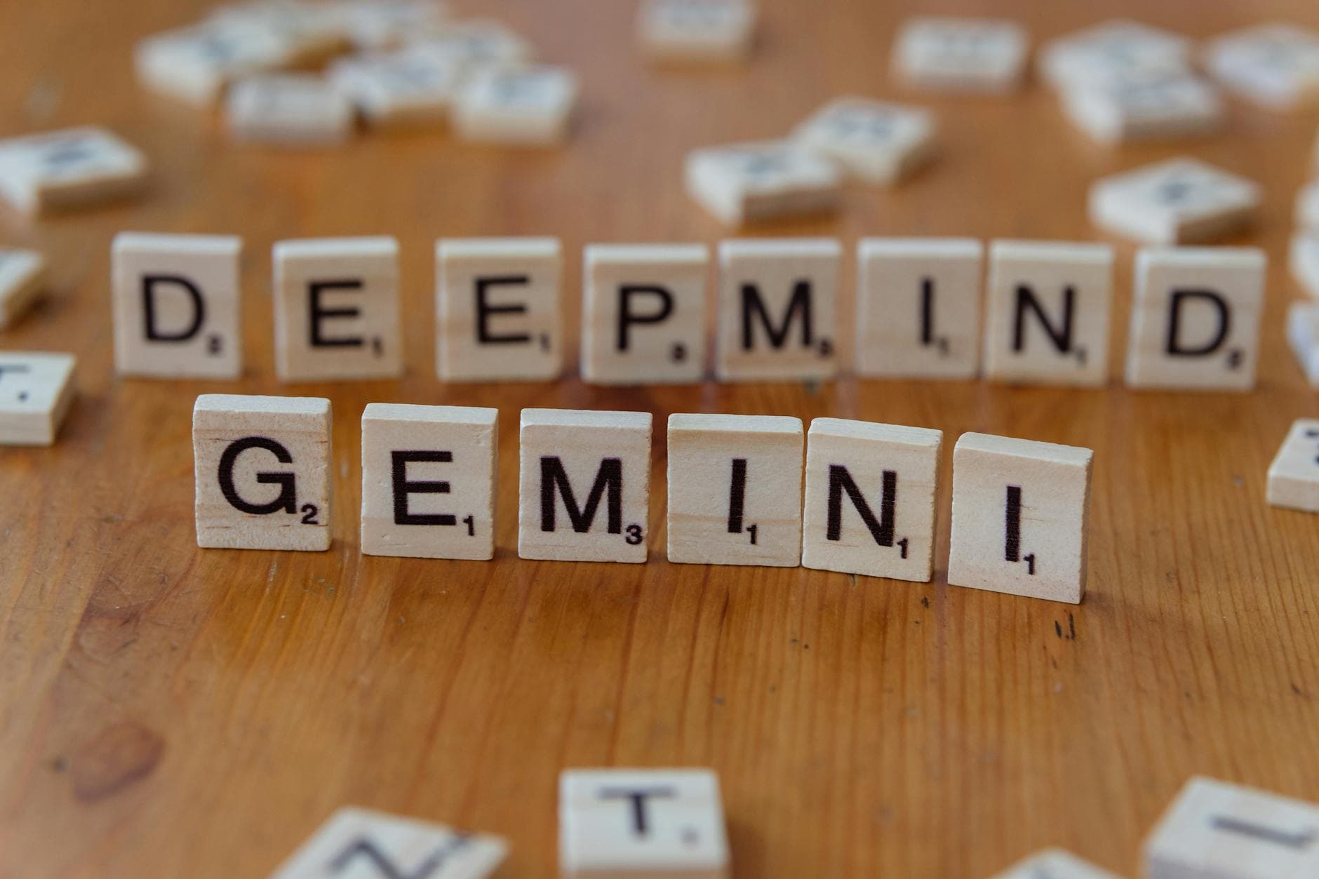 Wooden Scrabble tiles spelling 'Deepmind' and 'Gemini' on a wooden surface, a concept of AI and games.