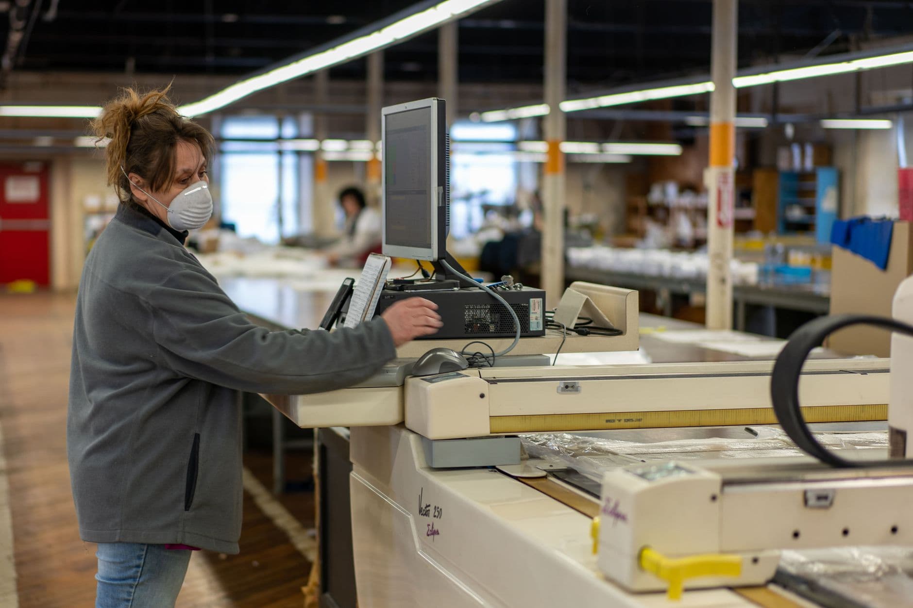 A woman operating machinery in a factory, wearing a safety mask for protection.