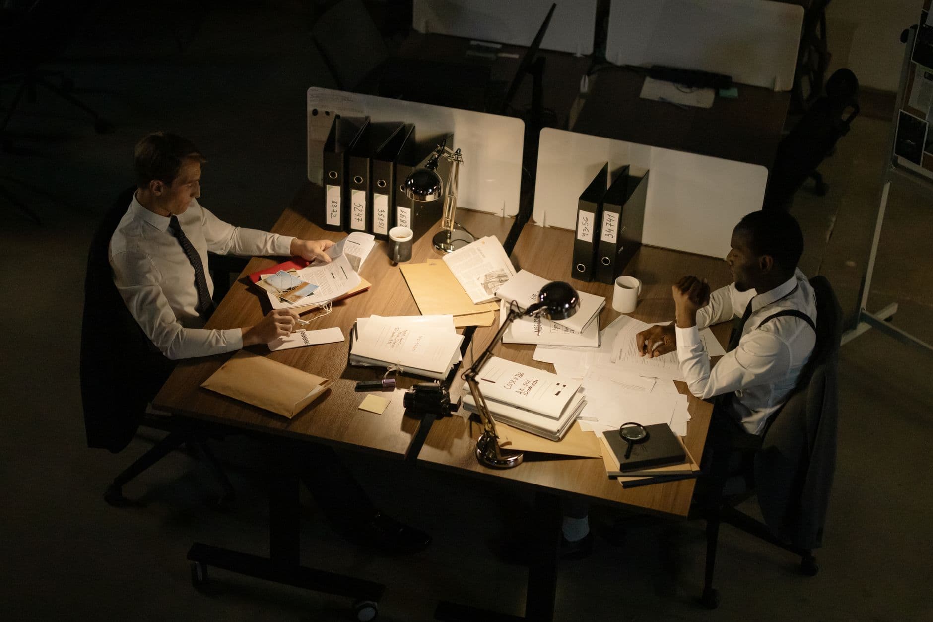 Two businessmen collaborating over documents in a dimly lit office setting.