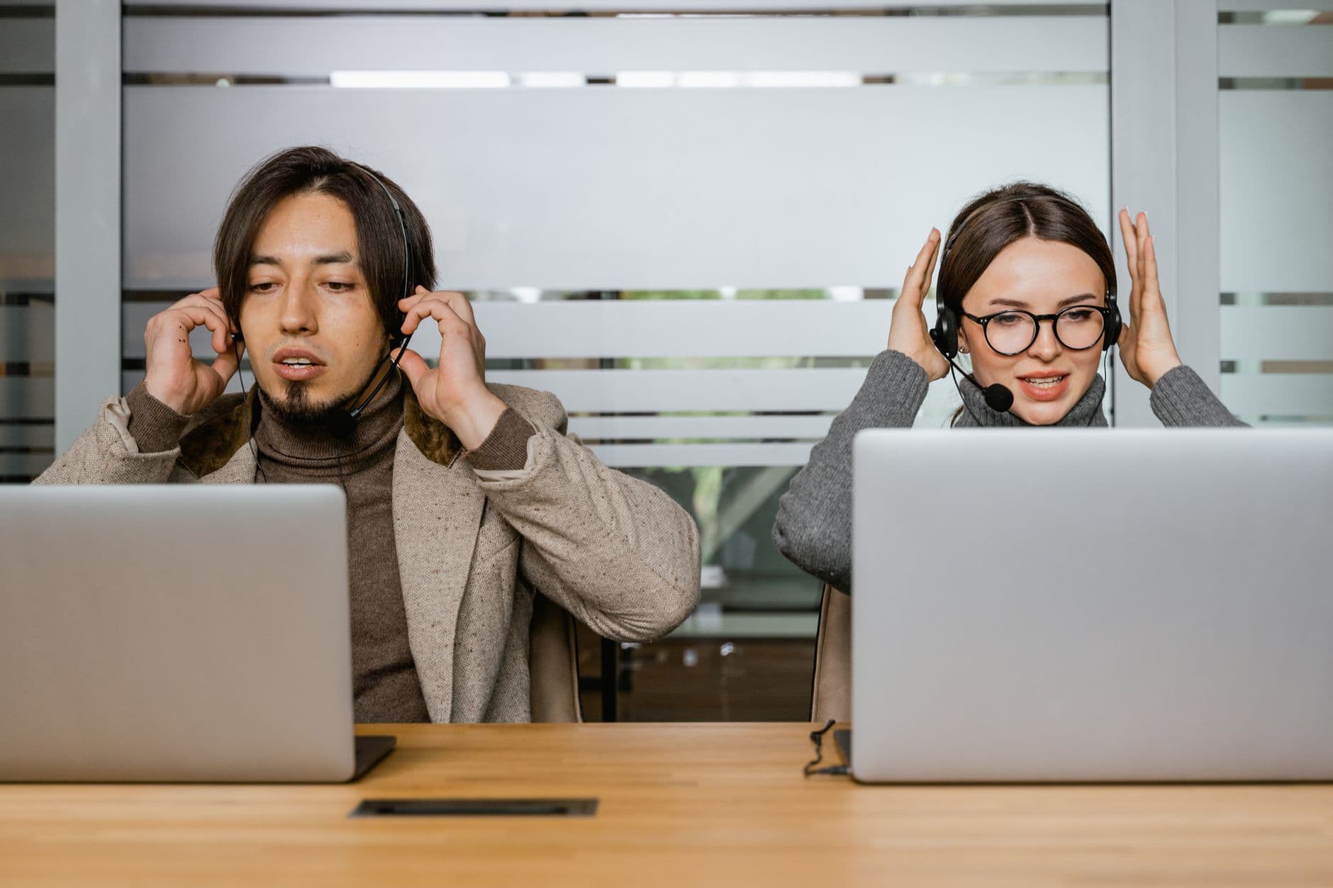 Two customer support agents using laptops and headsets in modern office.