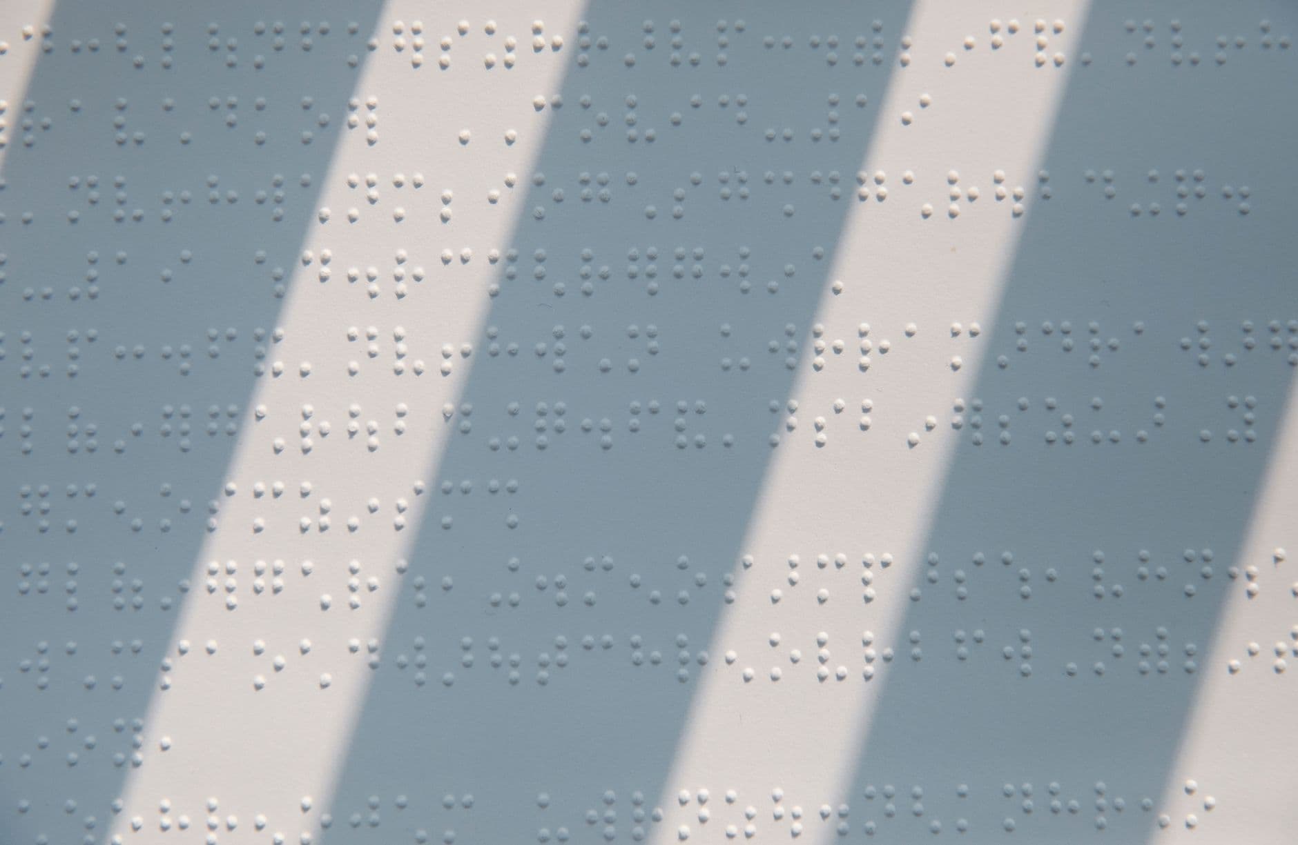 Close-up of braille text on paper with sunlight casting shadows, creating texture.
