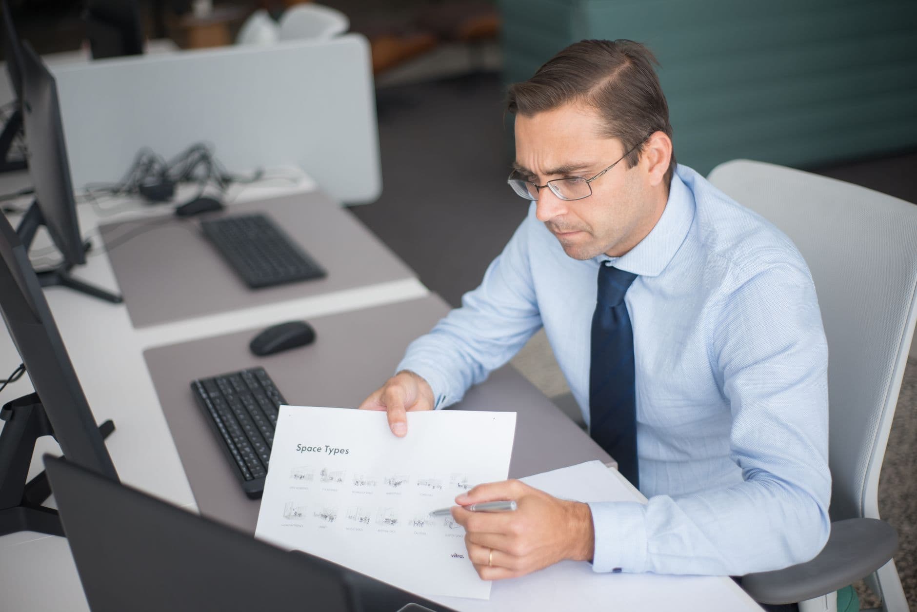 Businessman focused on analyzing documents at desk in office setting with computer.