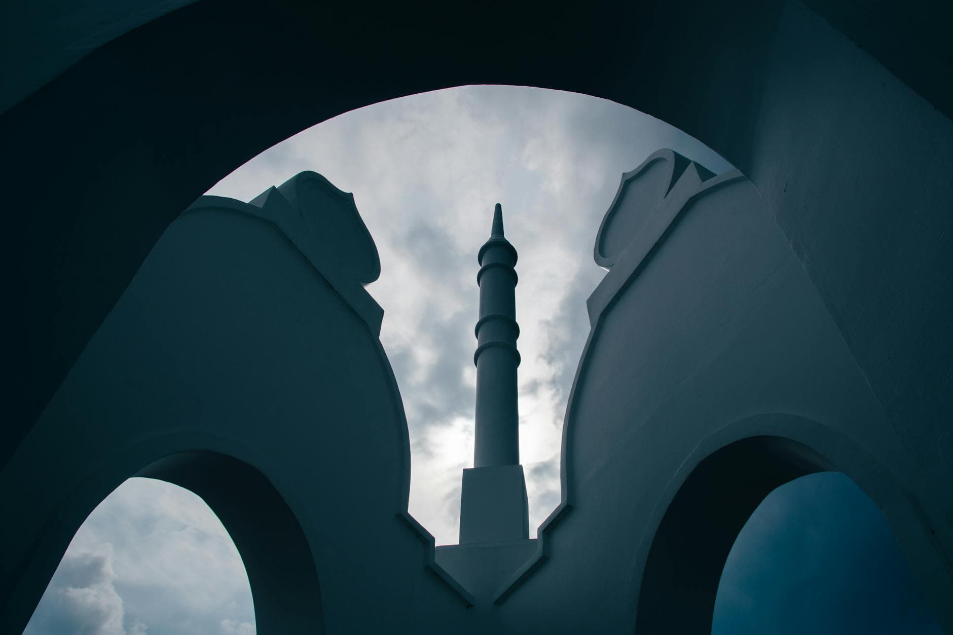 Silhouette of a mosque minaret framed by arches against a dramatic overcast sky in Banting, Malaysia.