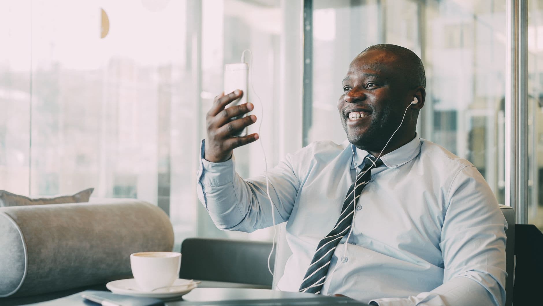 Smiling businessman on video call in a café, enjoying coffee.
