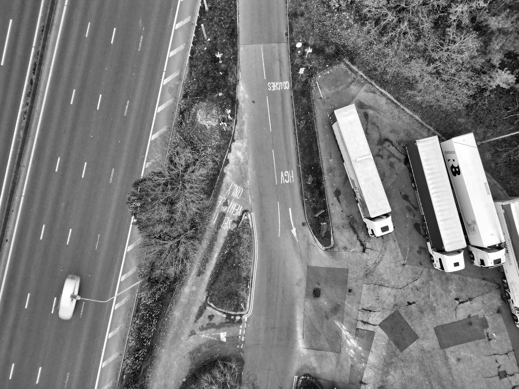 Aerial view of a highway intersection with parked trucks in black and white.