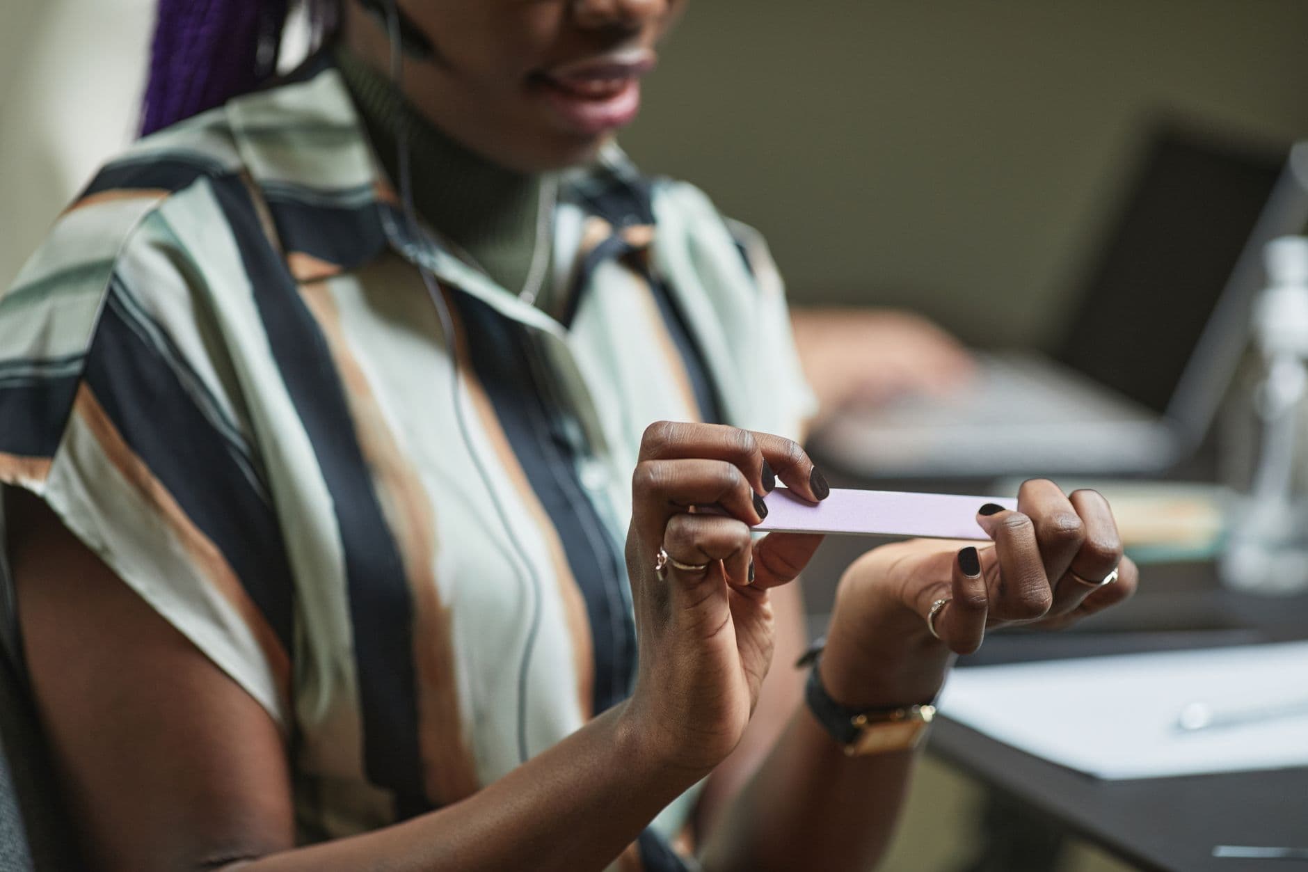 Close-up of a woman filing her nails while seated at her workplace. Modern office setting.