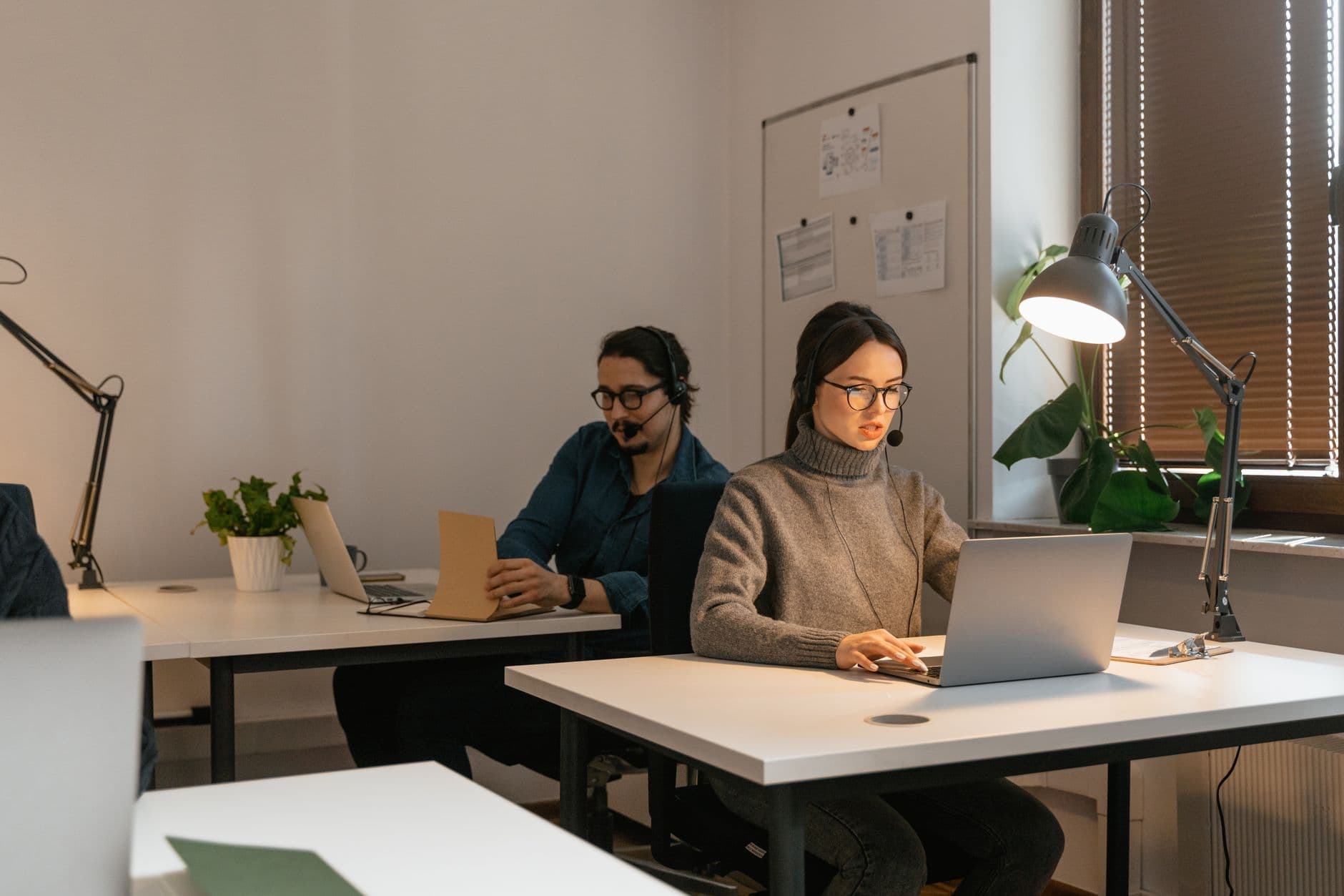 Two colleagues working in an office setting, focusing on laptops and customer support.