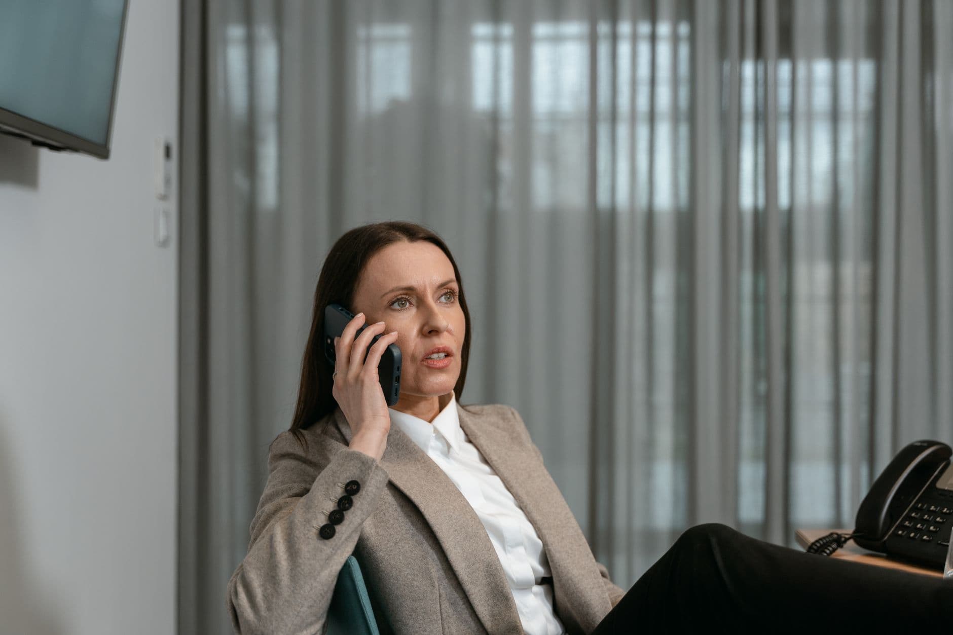 Businesswoman in a blazer engaged in a phone call in an office setting.