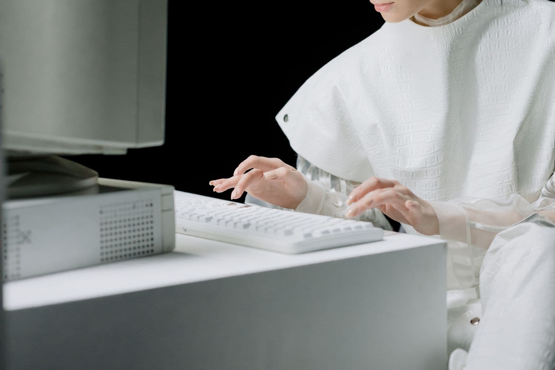 A woman in a white outfit typing on a white keyboard in a modern setting.