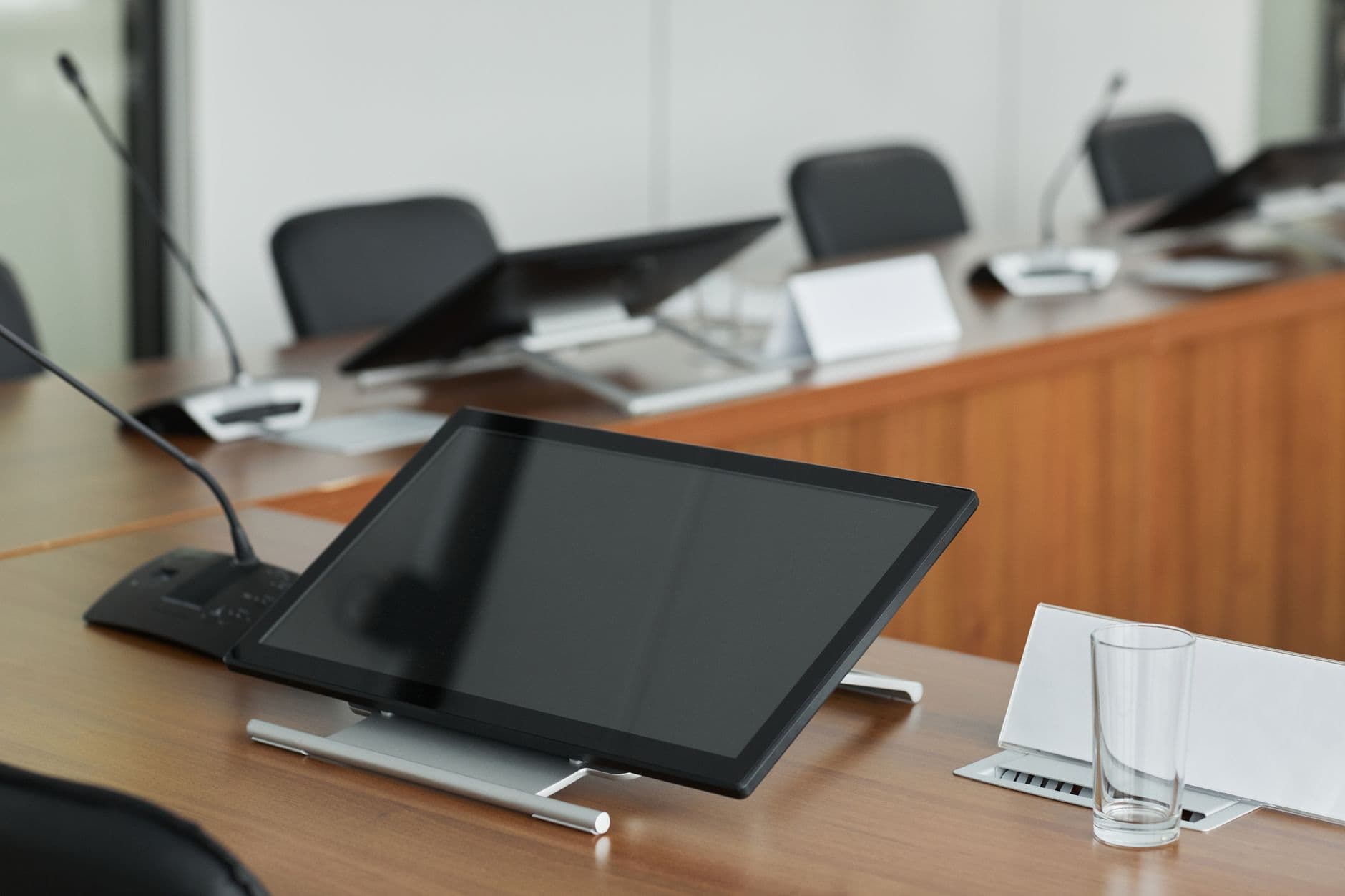 A modern conference room setup featuring digital monitors and microphones on a wooden table.