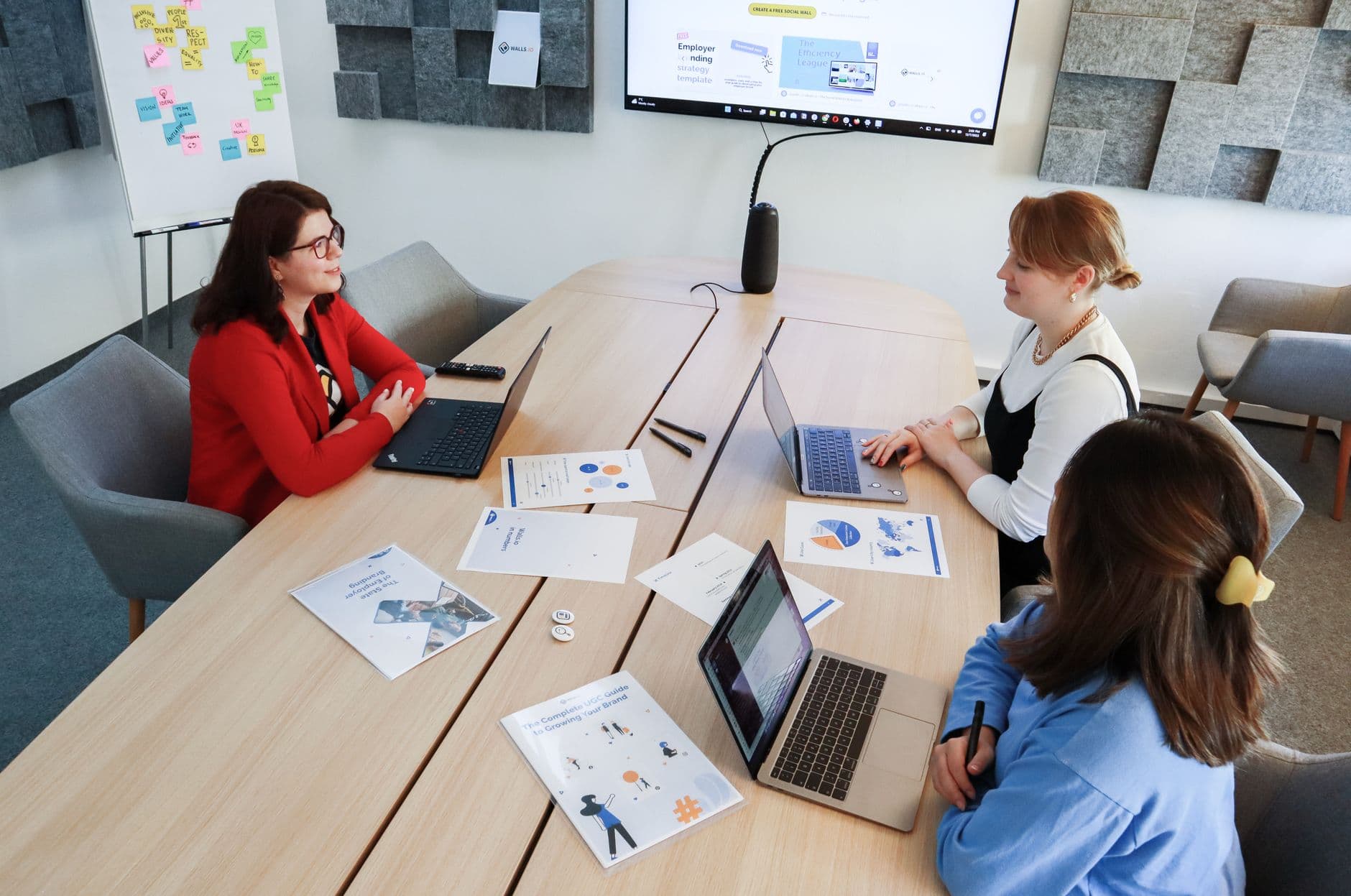 Three women in an office setting discussing business documents on laptops and paper.