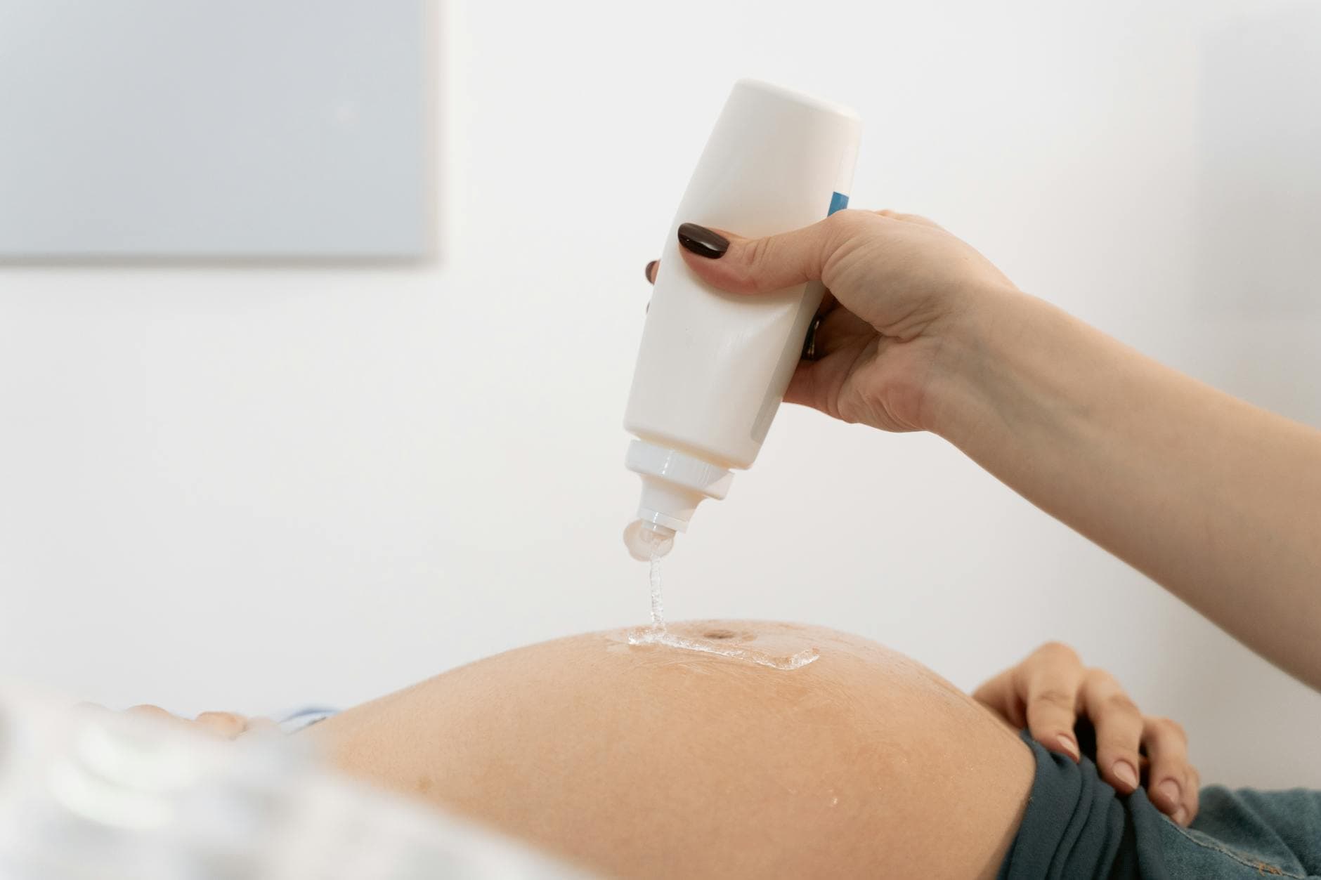 Close-up of a pregnant woman's belly with ultrasound gel being applied for a sonography session.