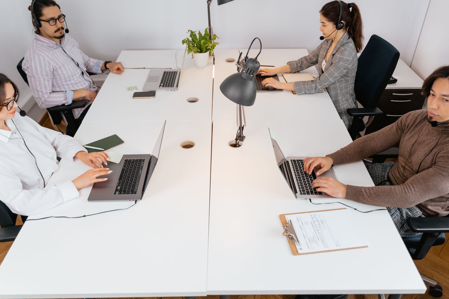 Team of four in a modern office setting using laptops and headsets for communication.
