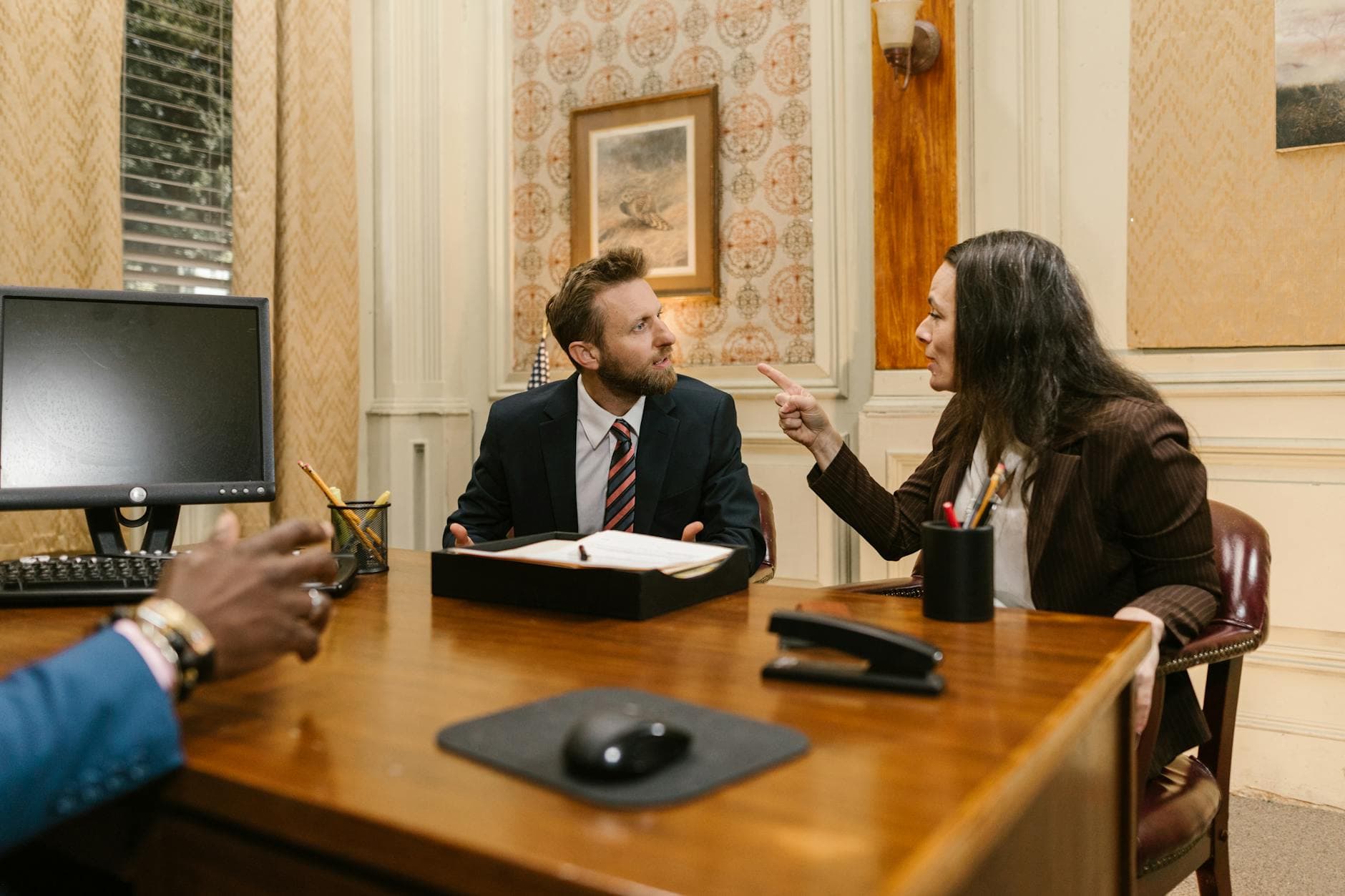 Professionals engaged in a serious discussion inside a law office with a computer on the desk.