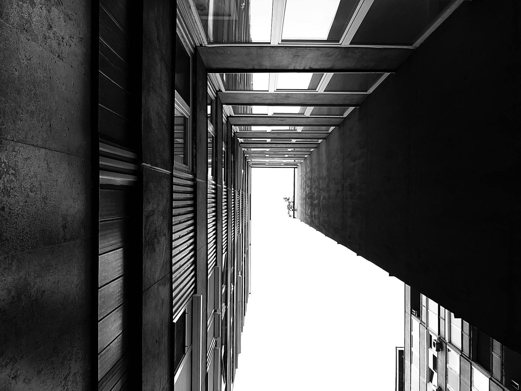 Black and white photo capturing a modern architectural corridor with glass and concrete elements.
