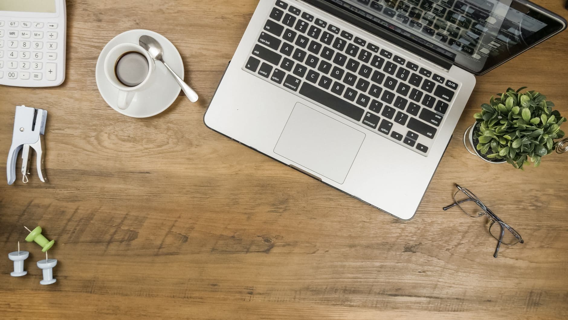 A flat lay of a tidy wooden desk with a laptop, coffee, and office supplies.