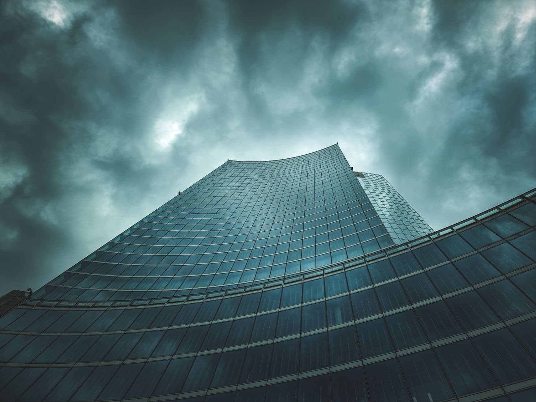 Low-angle view of a sleek skyscraper against a dramatic cloudy sky, showcasing modern architecture.