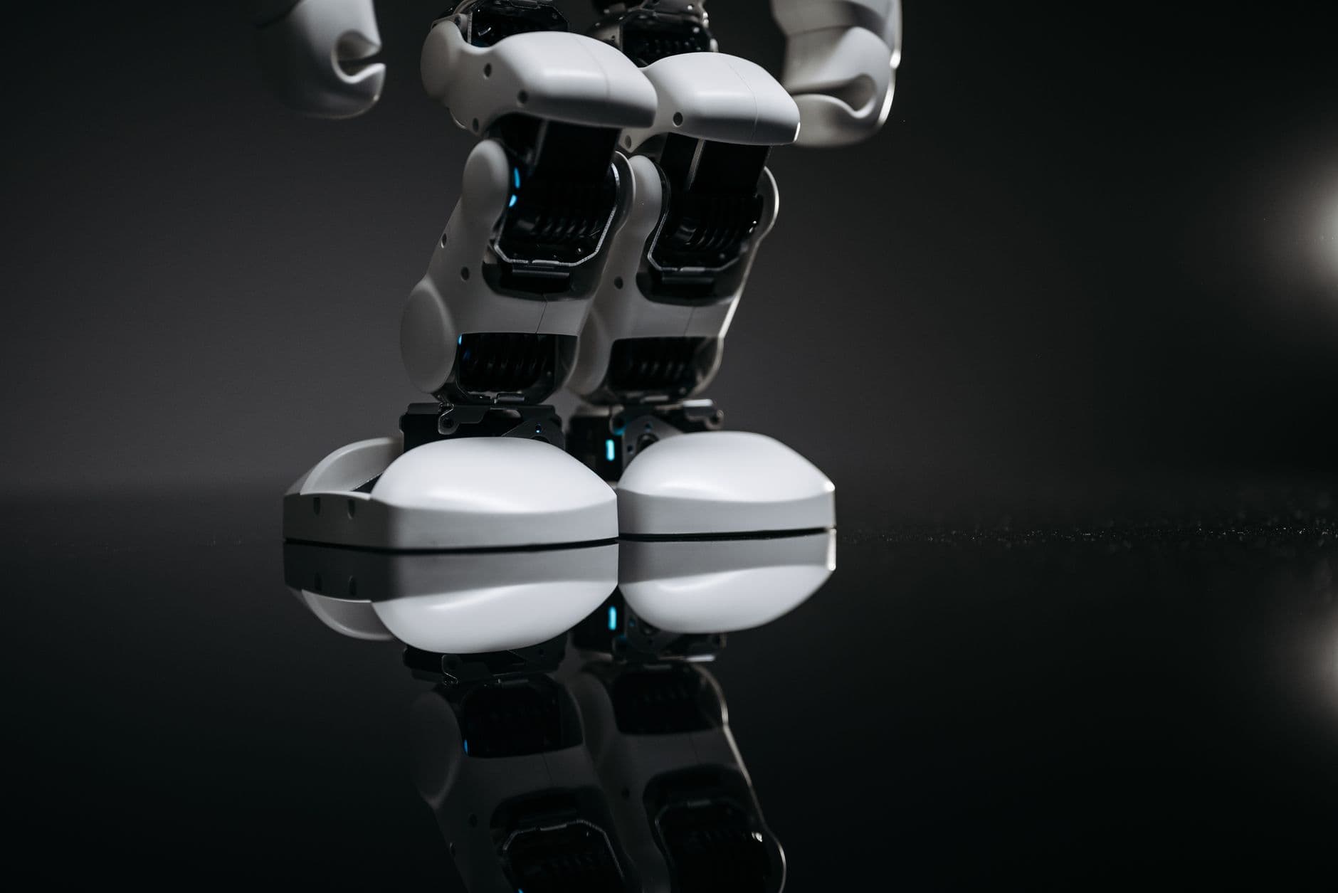 Close-up of robotic legs reflecting on a glossy surface in a studio setting.