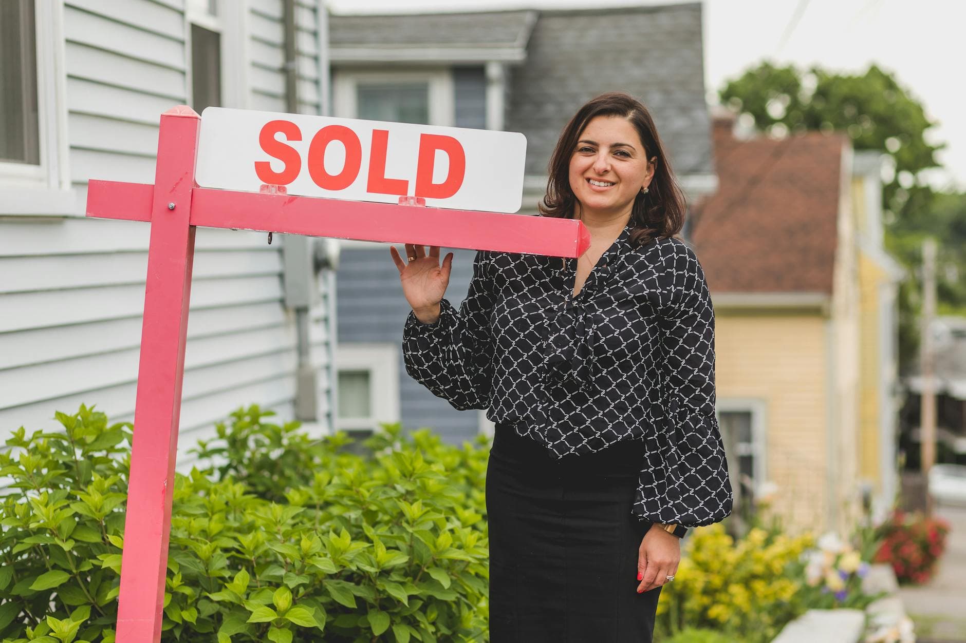 Smiling real estate agent standing outdoors with a sold sign, symbolizing success and achievement in property sales.