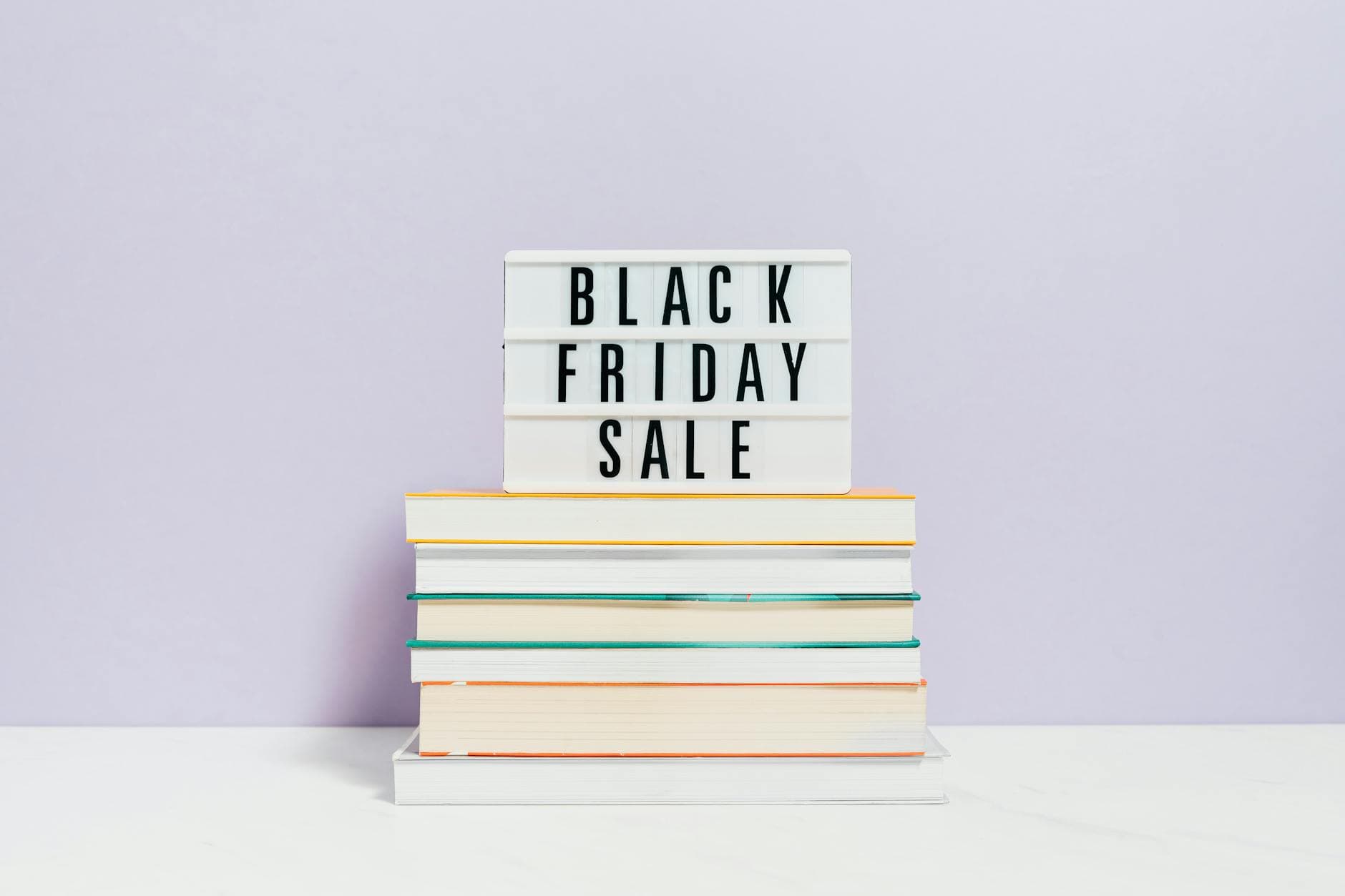 Stack of books with Black Friday sale sign on pastel background, perfect for retail promotions.