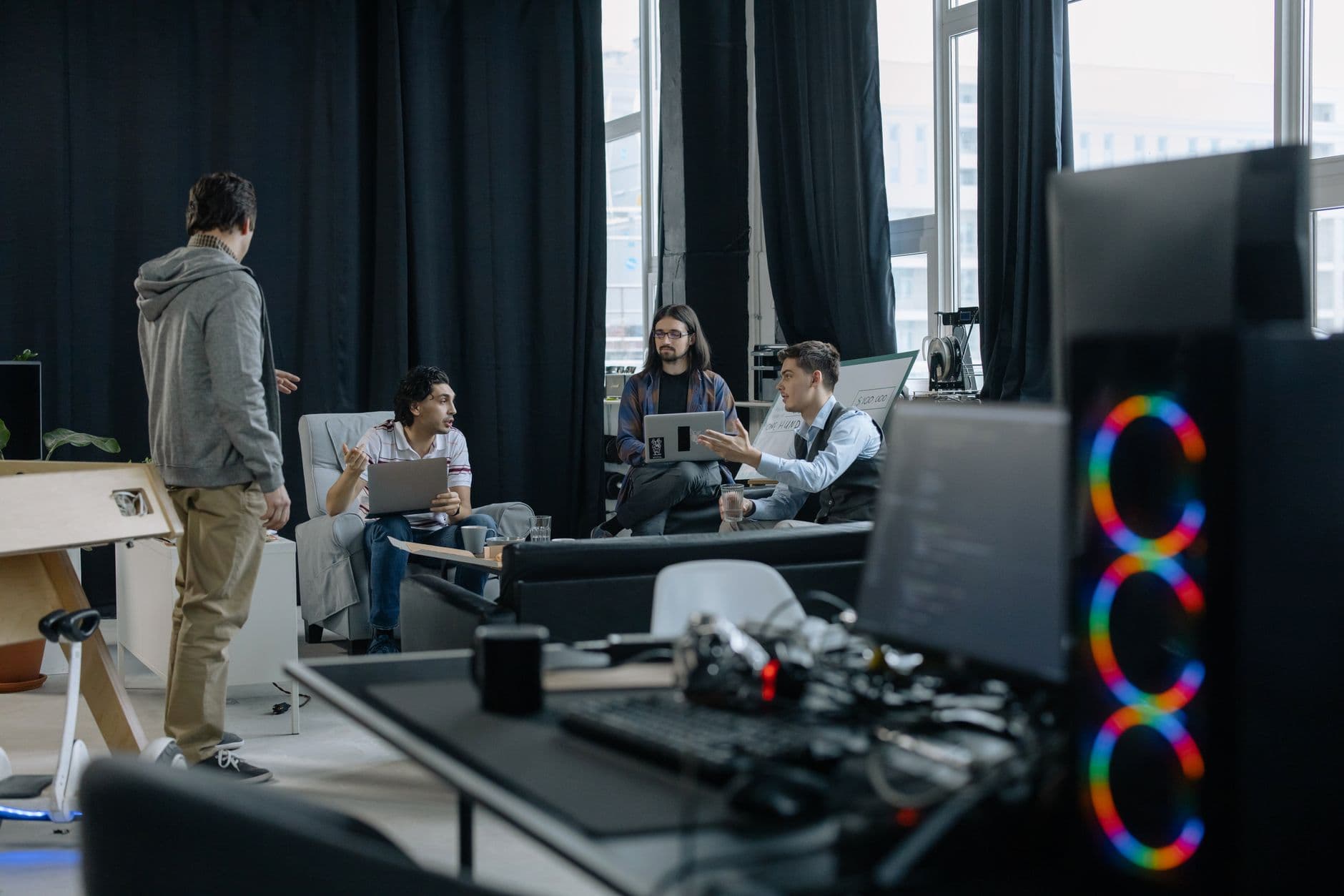 A group of professionals engaged in a casual meeting at a modern office, discussing projects on laptops and tablets.