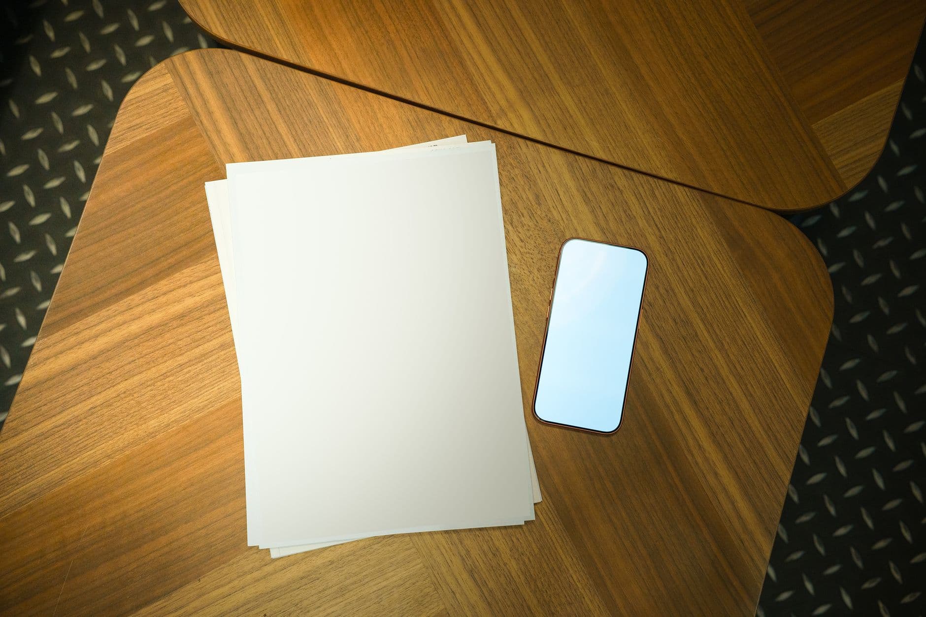 Top view of blank papers and a smartphone on a wooden table, perfect for business presentations.