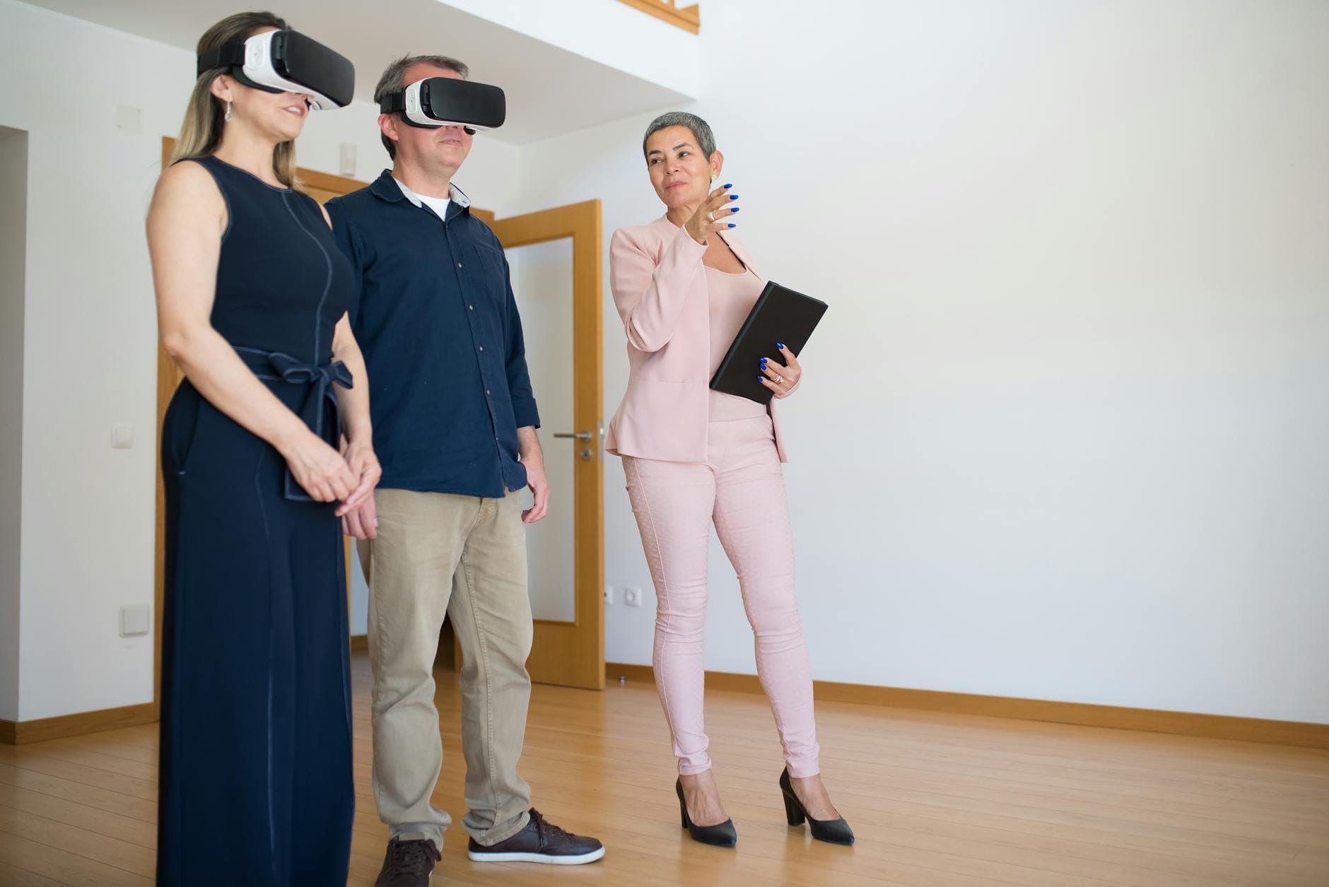 A couple uses virtual reality headsets for a house tour guided by a real estate agent indoors.
